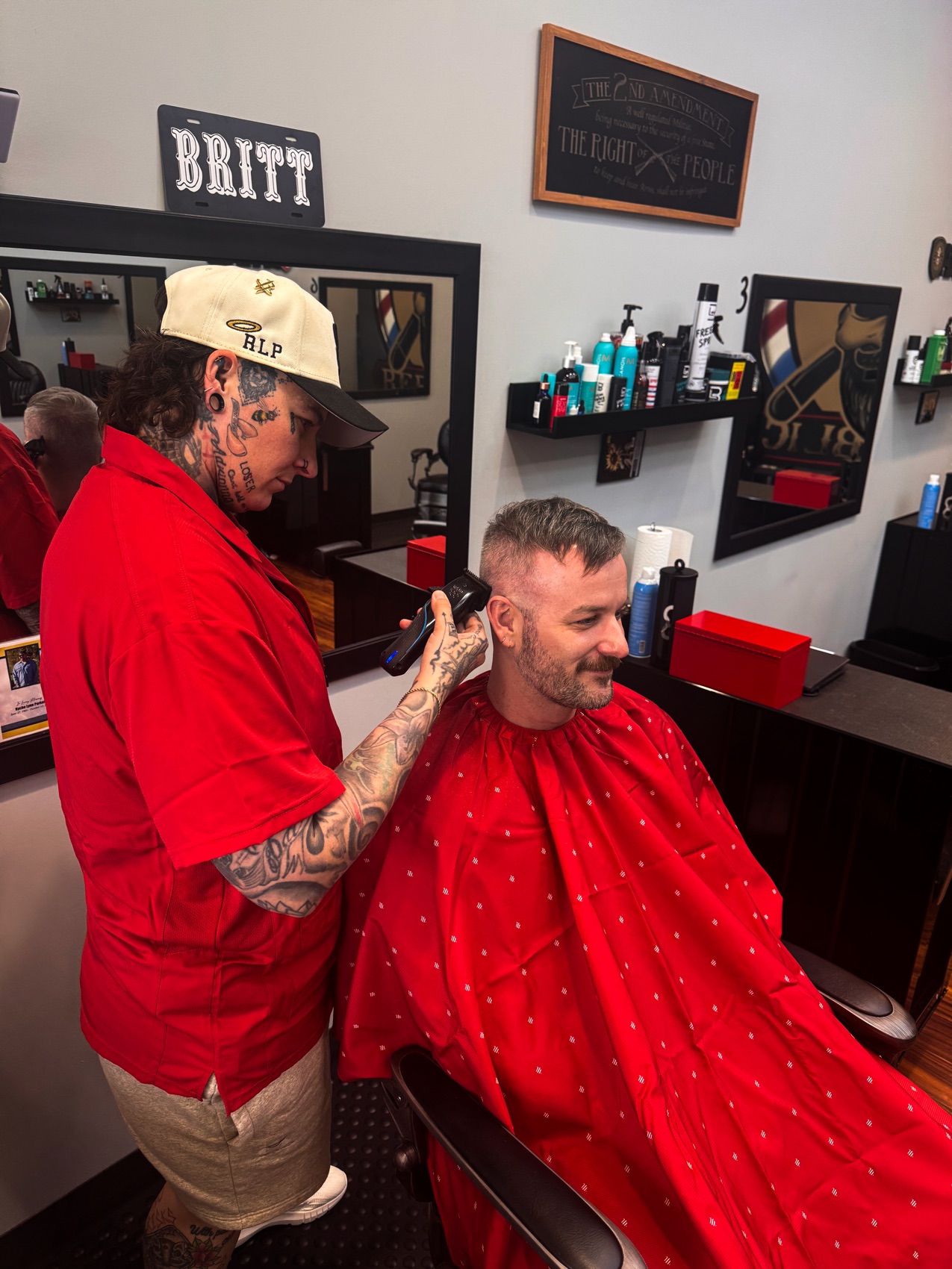 Brittany running clippers on a client in the red Razor Republic cape
